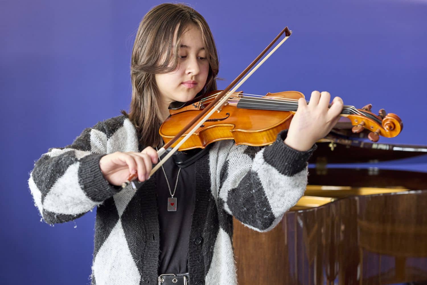 The alt text for the image showcases a talented young girl playing the violin in front of a beautifully crafted piano.