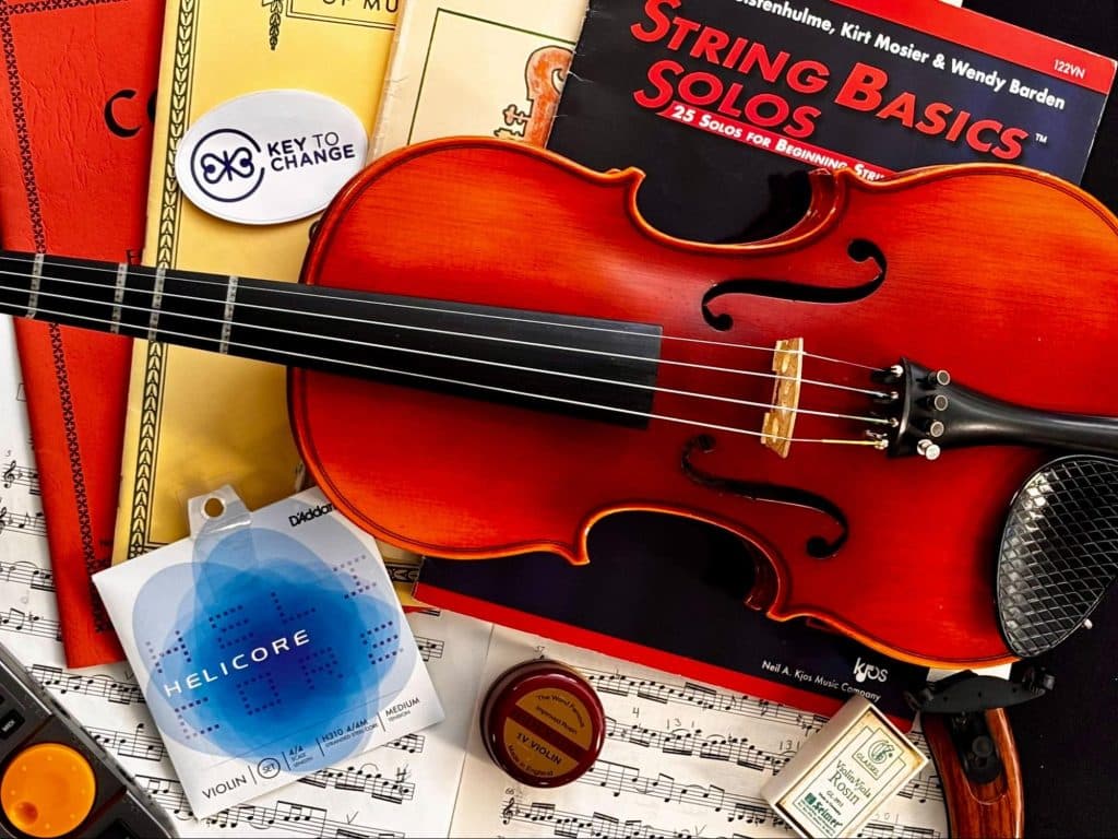 A photograph showing a violin, strings, rosin, and several music books used by students.